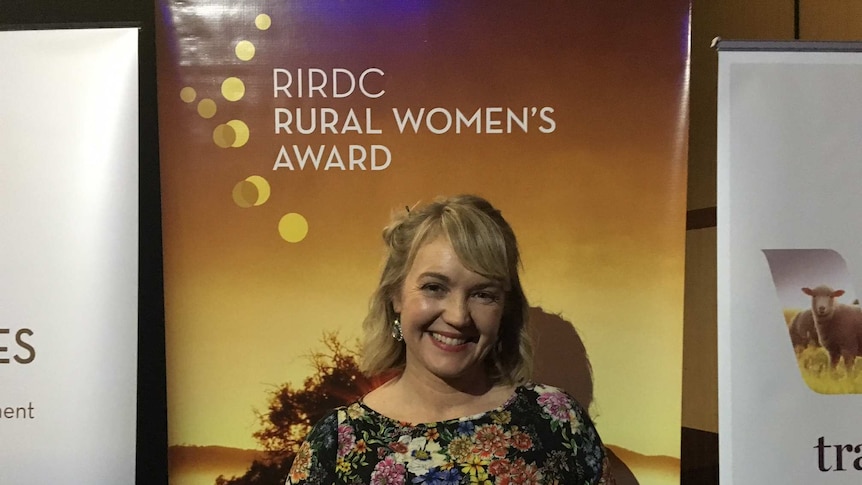 Woman smiles holding winning trophy for Rural Woman of 2016 in front of banner