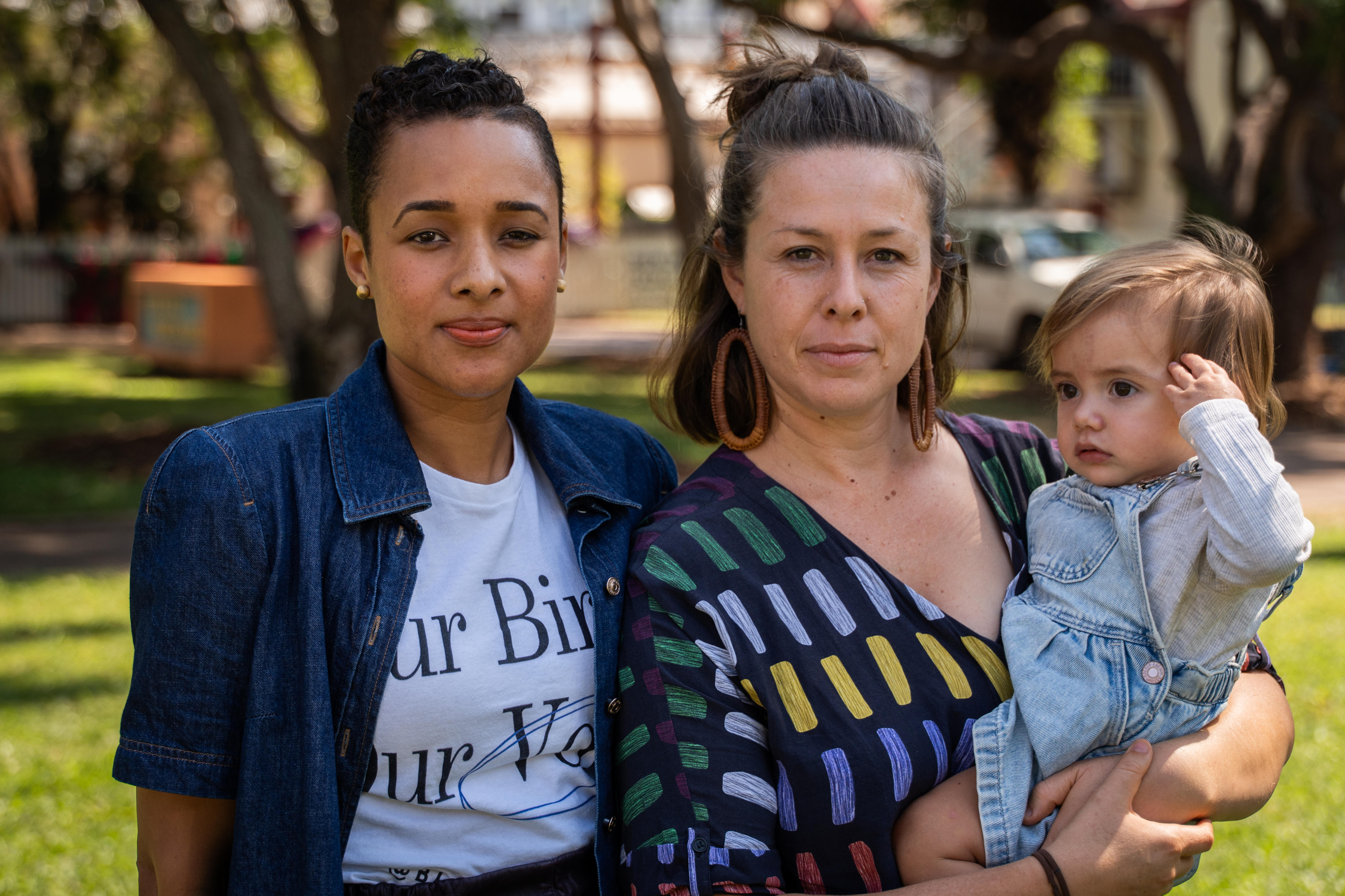 Two women, with one of them holding a small child, standing in a park and looking concerned.