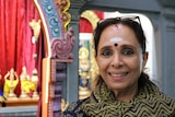 A woman with religious bhindi smiles, she is inside a Hindu temple.