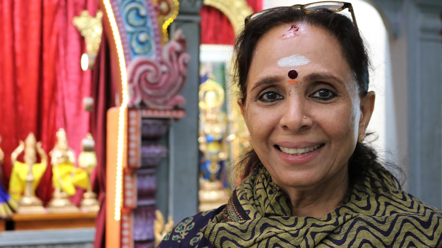 A woman with religious bhindi smiles, she is inside a Hindu temple.