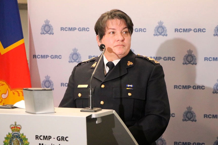 Female police officer stands behind a podium speaking during a press conference