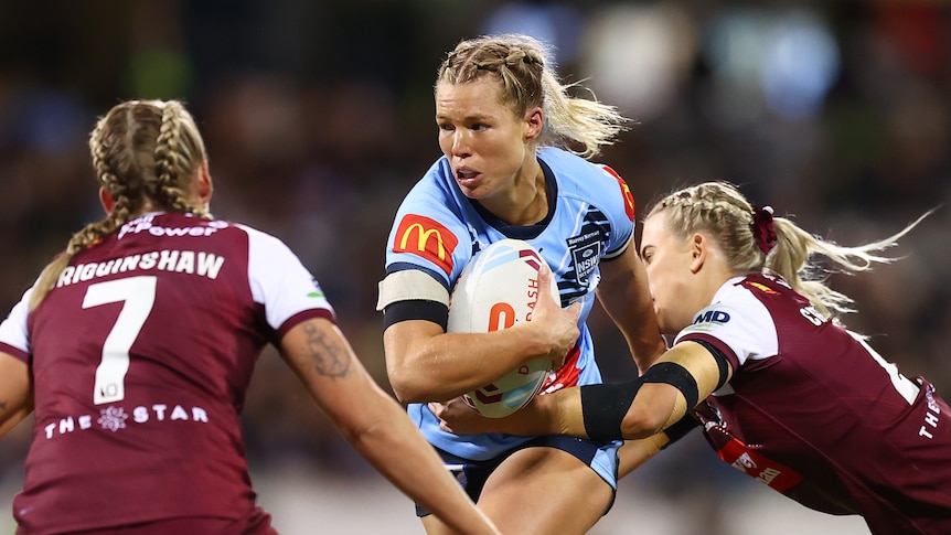 Emma Tonegato runs with the ball under her arm as two Maroons defenders attempt to tackle her