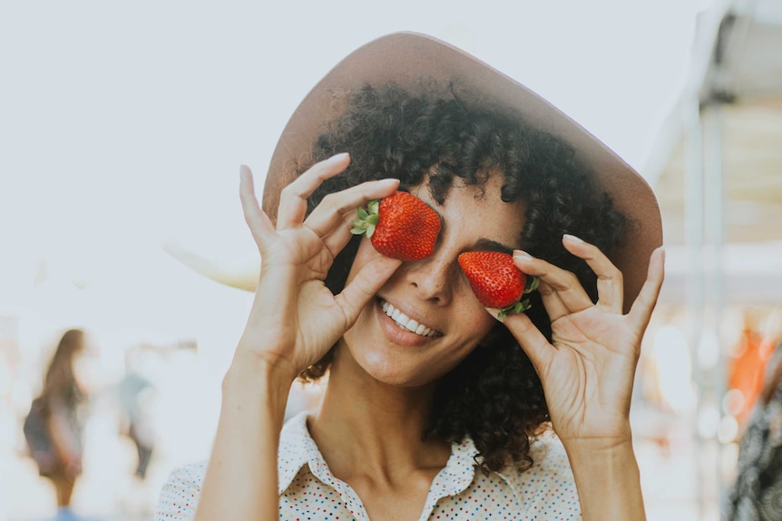 A woman holding strawberries over her eyes to depict information about how to choose fresh fruit and vegetables.
