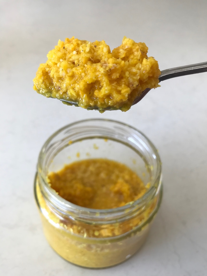 A teaspoon of turmeric tonic, a minced yellow paste above a glass jar. 
