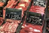 Lamb ribs and lamb steaks sit in a butchers counter with price tags above them