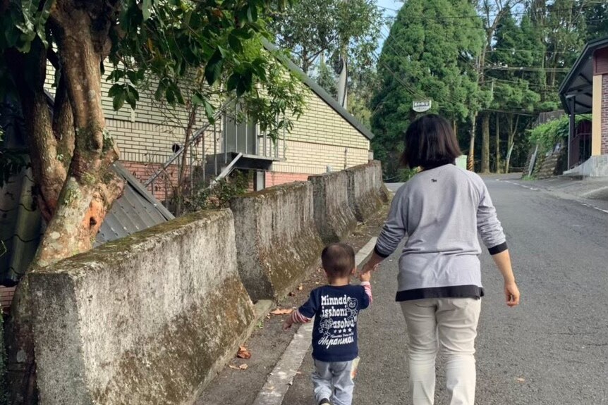 Yuke Chen's mother walks down the street in a quiet residential area holding hands with a toddler.
