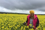 A girl standing in a yellow canola crop under a cloudy sky holding a camera