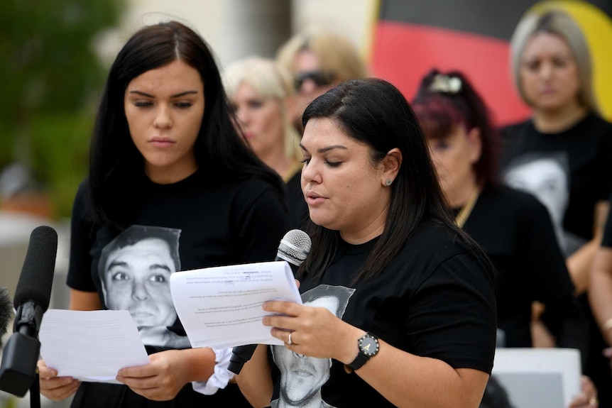 two women reading a speech while the Aboriginal flag flies behind them