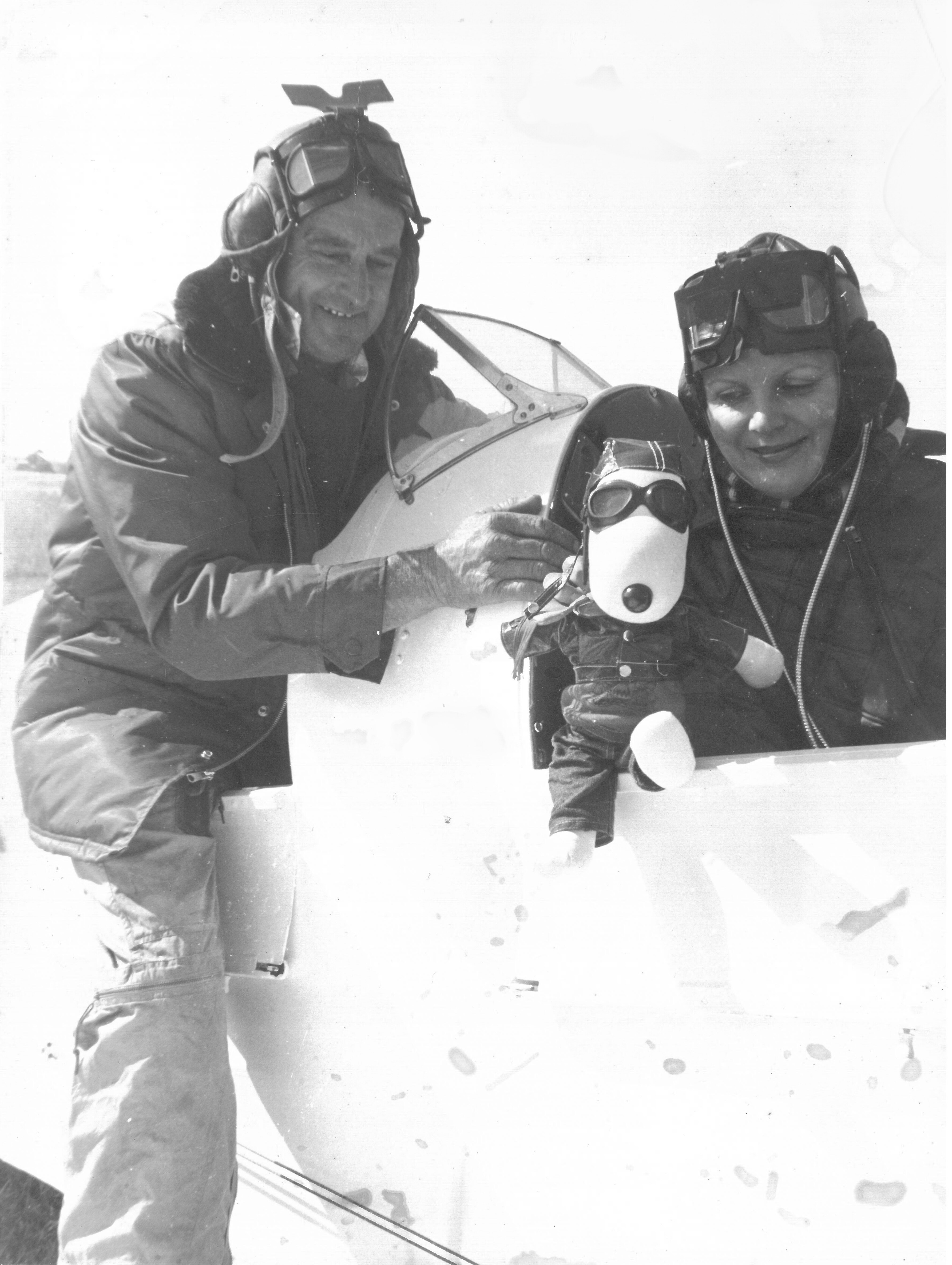 On old photo of a couple gathered by a small plane. The woman is holding a stuffed animal