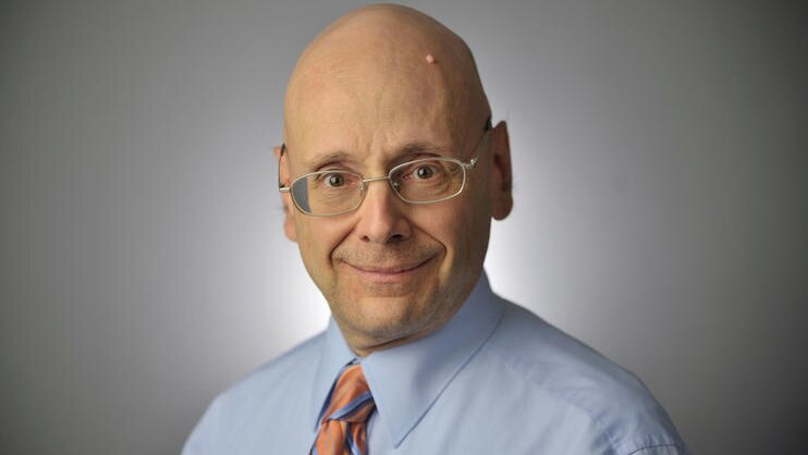 Gerald Fischman wearing a blue shirt with an orange and blue striped tie.