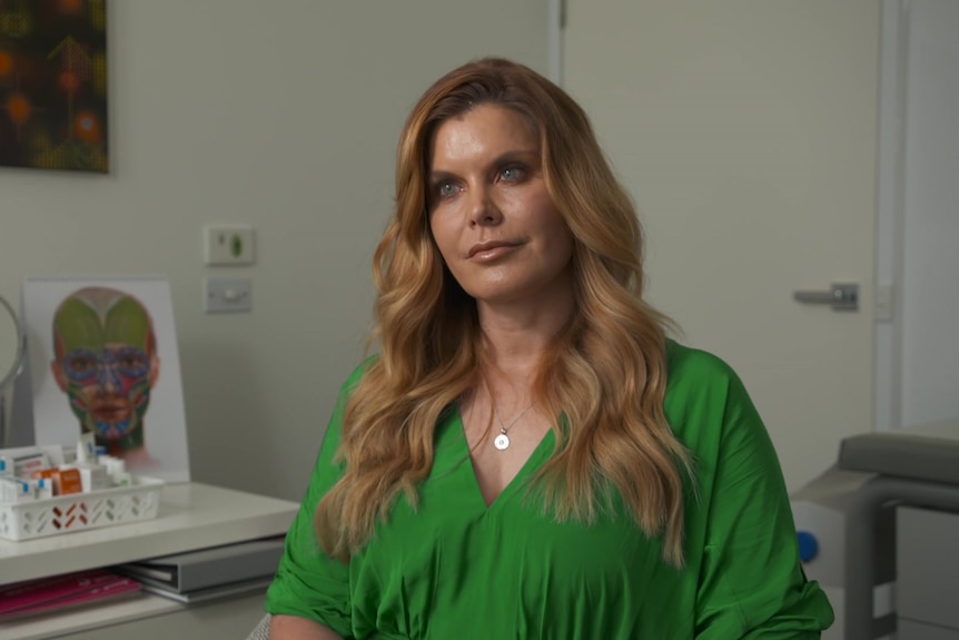 Woman in a green shirt with long brown hair sitting in a dermatologist office.