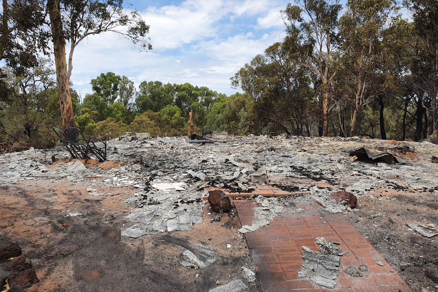 Charred remains of a building against a bush backdrop.