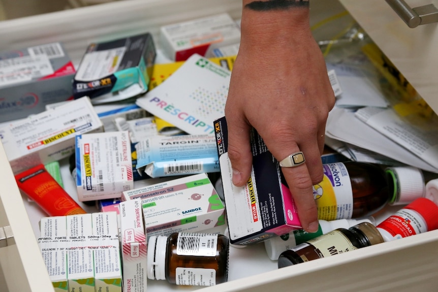 A hand reaches into a drawer filled with medications, and grabs a box.