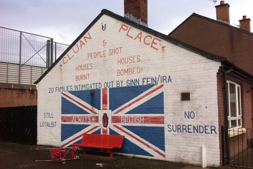 A mural painted onto the side of a gable-house roof reads 'still loyalist 'no surrender' around a Union Jack.