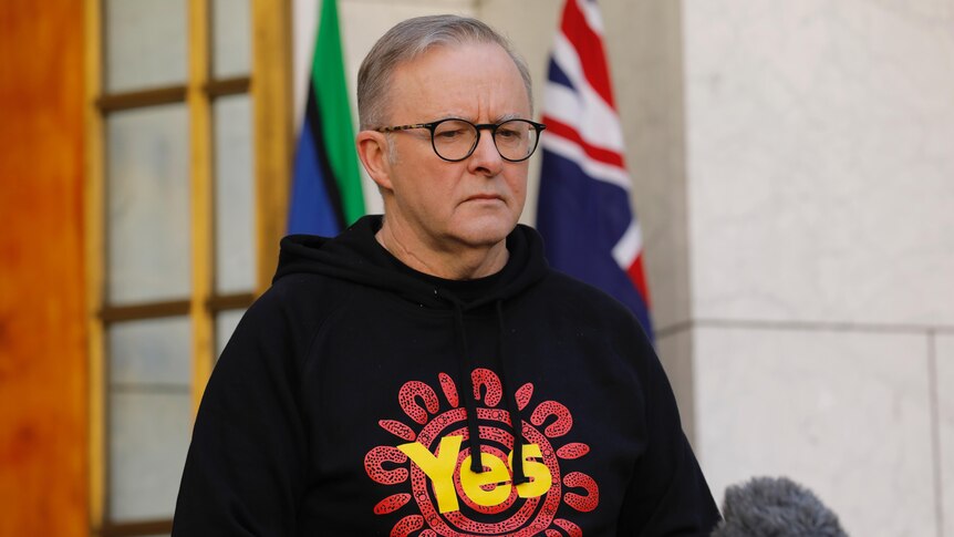 Albanese stands wearing a "Yes" Voice hoodie in the prime minister's courtyard, looking serious.