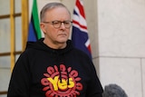 Albanese stands wearing a "Yes" Voice hoodie in the prime minister's courtyard, looking serious.