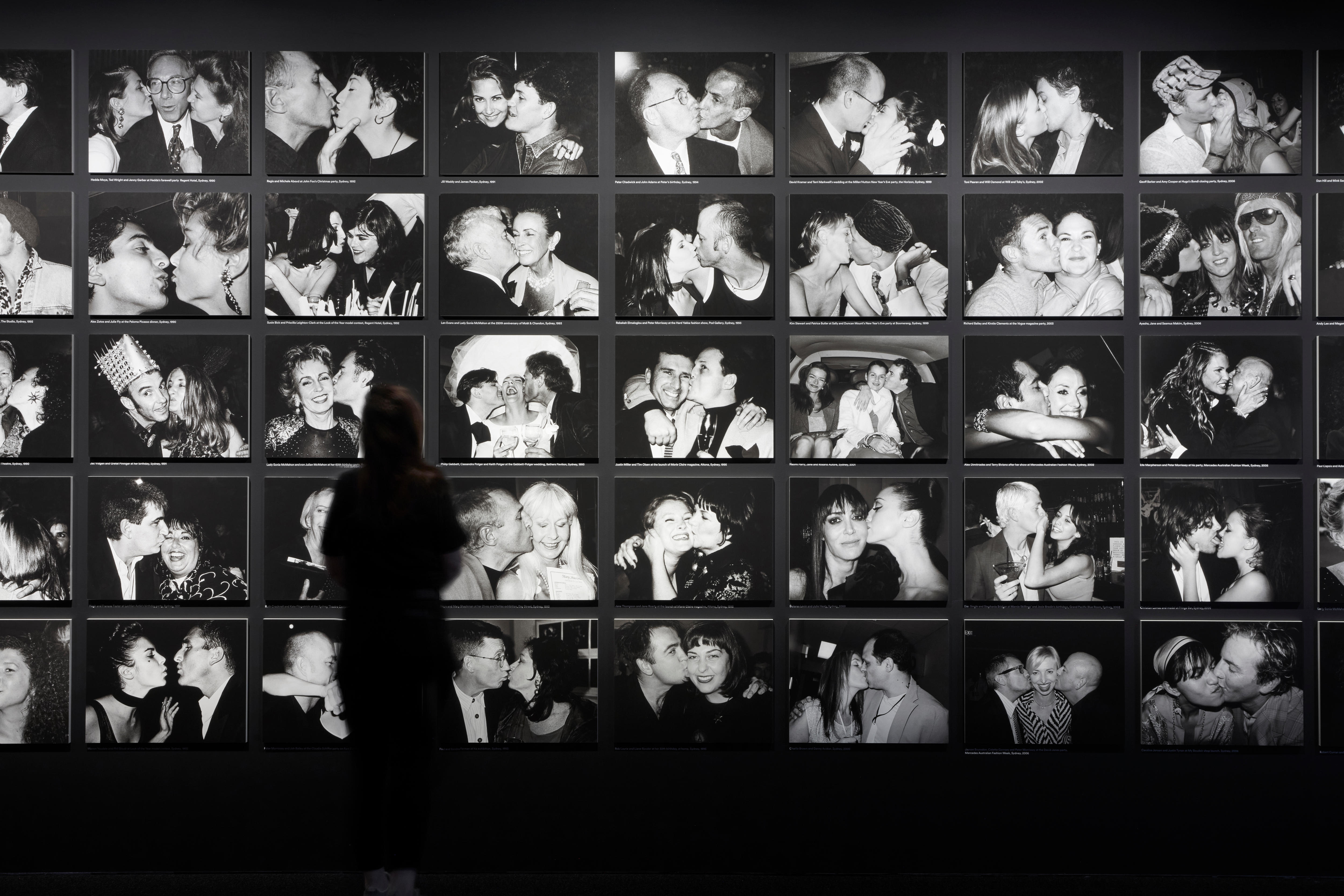 A person stands in front of a display of old black and white portraits of celebrities hugging and kissing. 