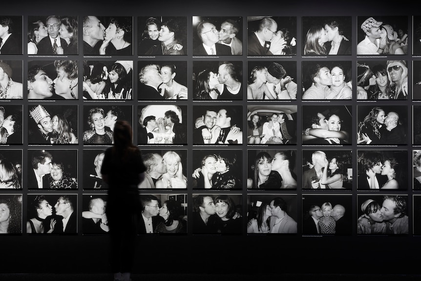 A person stands in front of a display of old black and white paintings of celebrities embracing and kissing. 