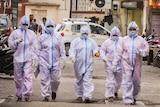 A group of health workers in full PPE walk down a street