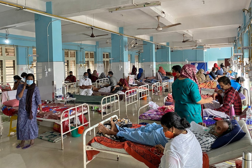 A hospital ward full with a number of beds with people on oxygen machines.