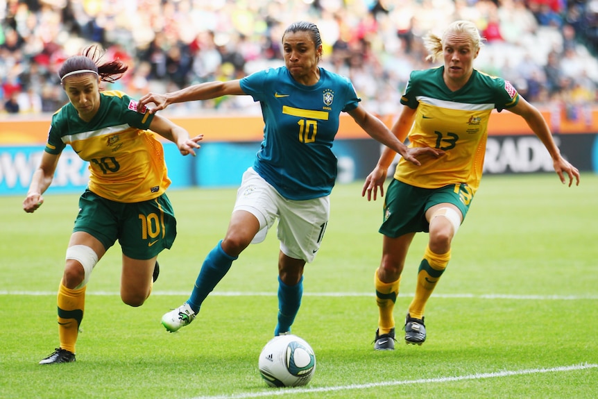 Marta Vieira da Silva fends off two Australian players while kicking a soccerball.