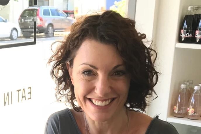 MIddle aged woman with brown curly hair smiles at the camera 