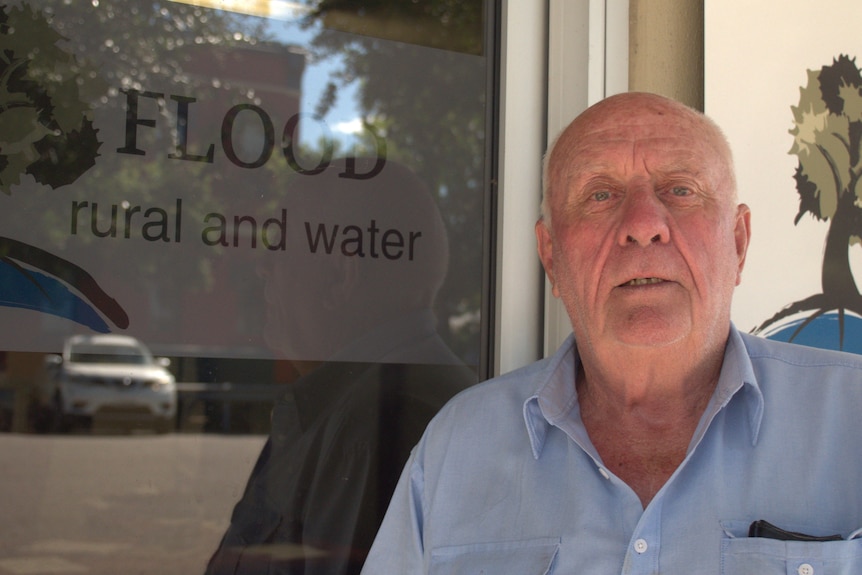 An older man stands in front of a door.