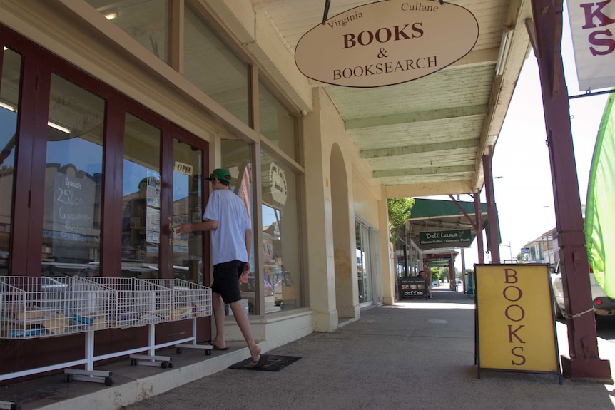 A young man walks into a bookshop in an old shop with wooden verandah posts