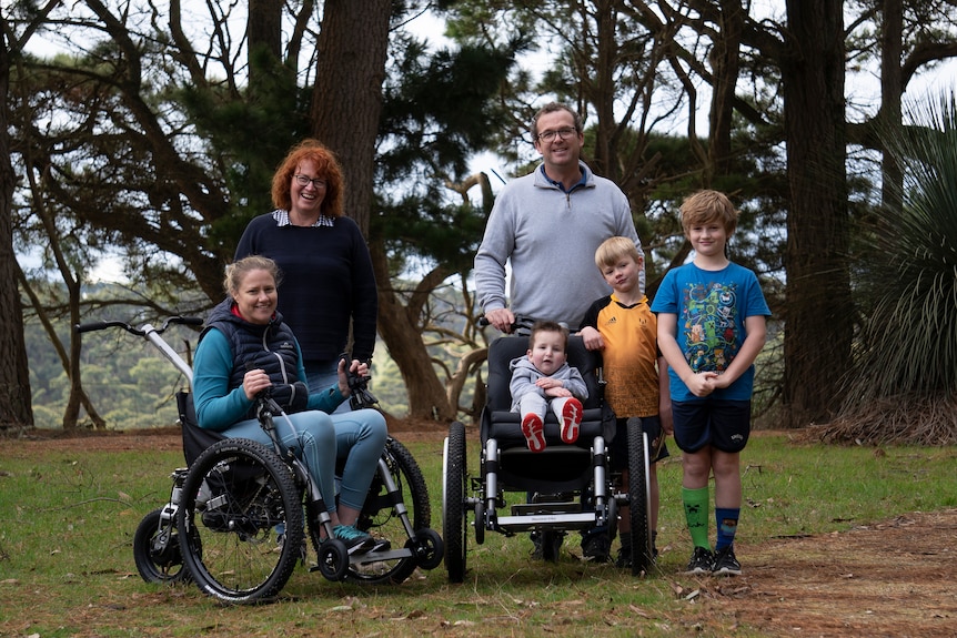 Yvette Eglinton with her family, a man and two boys, while a toddler sits in a pram. A red-haired woman stands near.