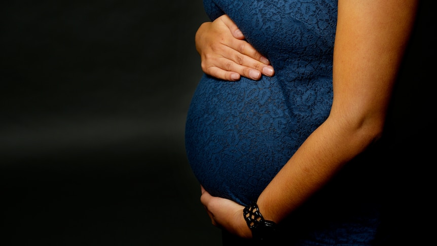 a close-up of a woman's pregnant belly. she has one hand underneath her belly and one on top of it