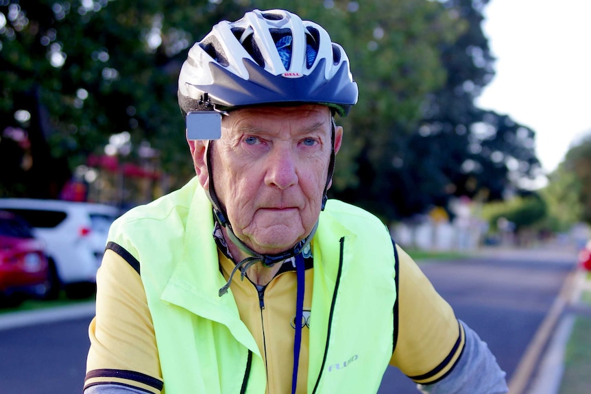 An elderly man on a bike wearing a helmet and high-visibility vest.