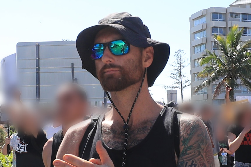 A man wearing a black singlet and a black floppy hat, with a sleeve tattoo on his left arm