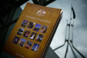 A pocket edition of the Australian constitution held against a window. In the background, Parliament House's flag is visible