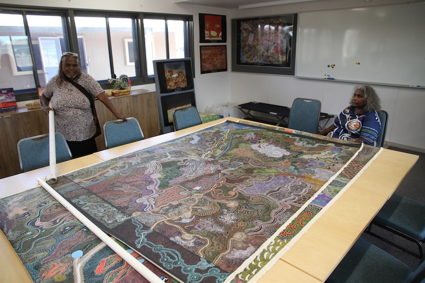 The painting is spread out on a table which two women stand near