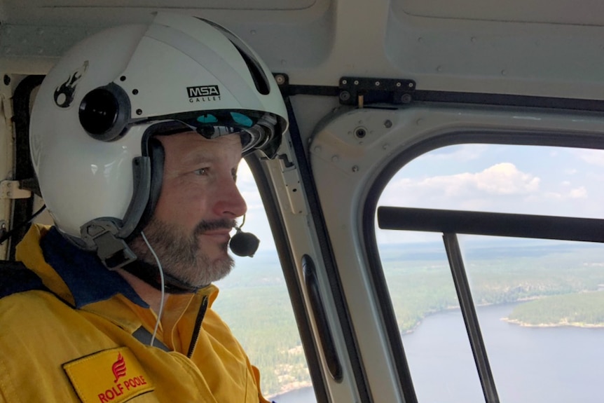 Fire inspector in a helicopter, a headshot from the side. He's wearing a helmet and fire gear