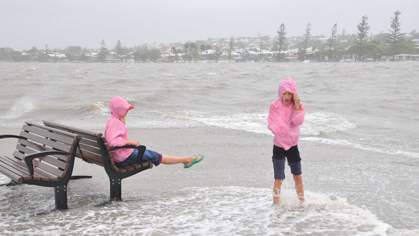Two young girls relax on the end of the Wynnum Jetty in Brisbane at high tide, as wild weather strikes the state.