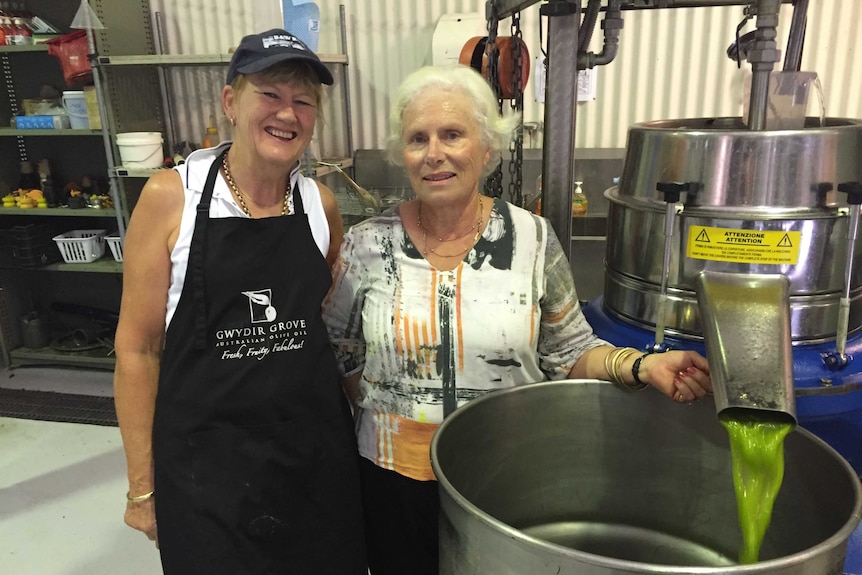 Jenni Birch and Margi Kirkby, Gwydir Grove, stand beside freshly processed olive oil pouring from a processing unit