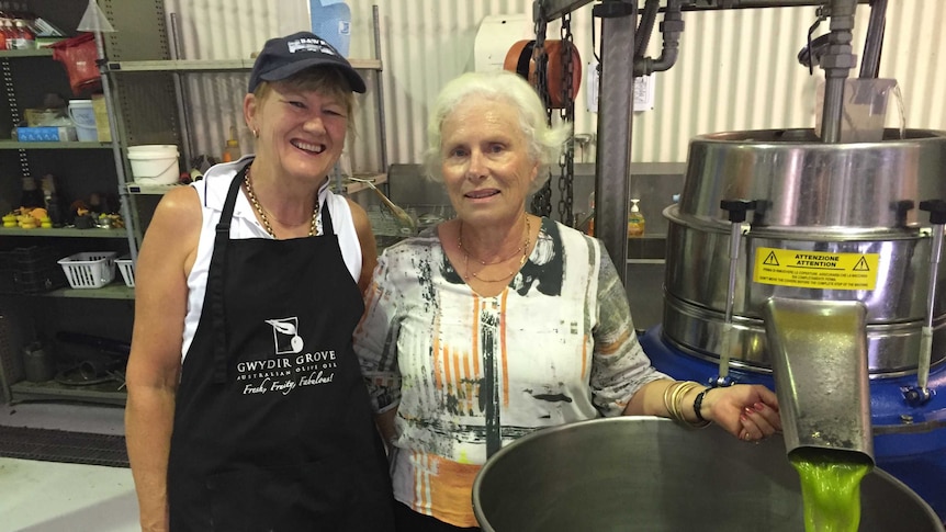 Jenni Birch and Margi Kirkby, Gwydir Grove, stand beside freshly processed olive oil pouring from a processing unit