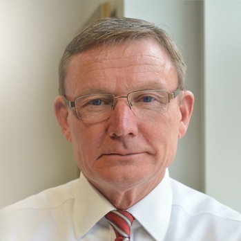 Paul Symon, wearing a glasses, stares down the barrel of the camera for a portrait photograph.