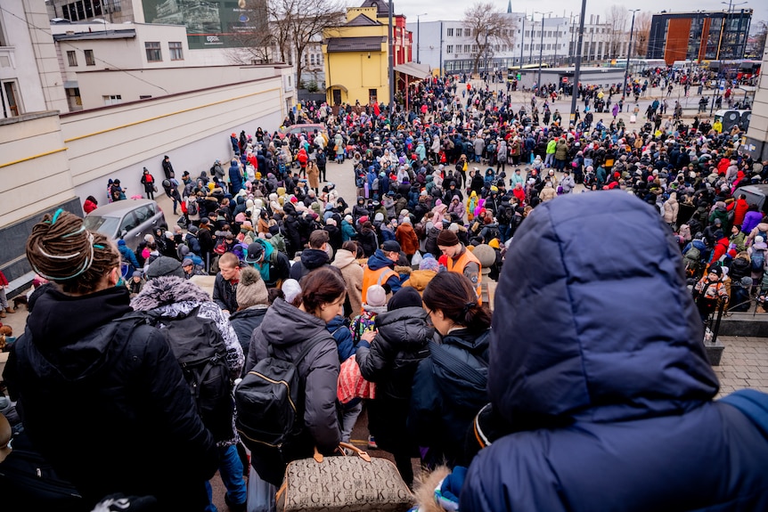 A large crowd of people in winter clothes and holding luggage at Lviv train station in Ukraine.