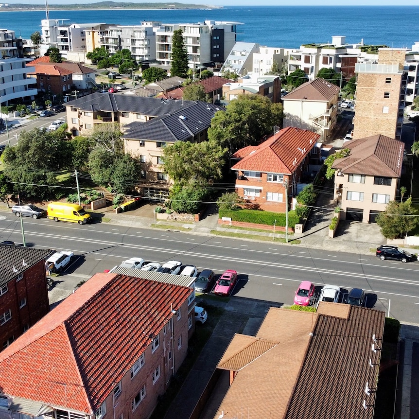 A bird's eye view of unit blocks and apartments with the ocean in the background on a sunny day.