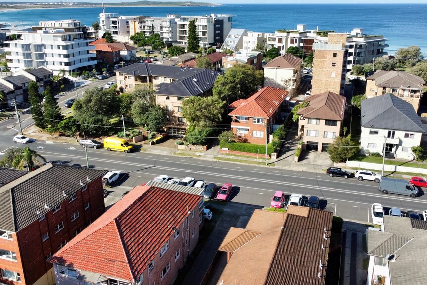A bird's eye view of unit blocks and apartments with the ocean in the background on a sunny day.