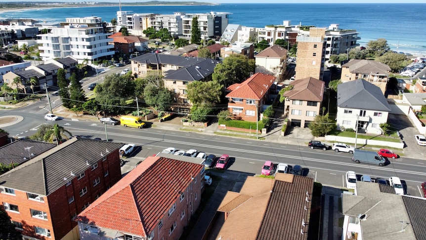 A bird's eye view of unit blocks and apartments with the ocean in the background on a sunny day.