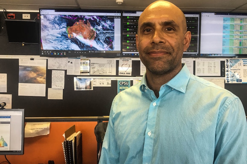 A man stands in front of an image of cloud cover over a map of Australia.