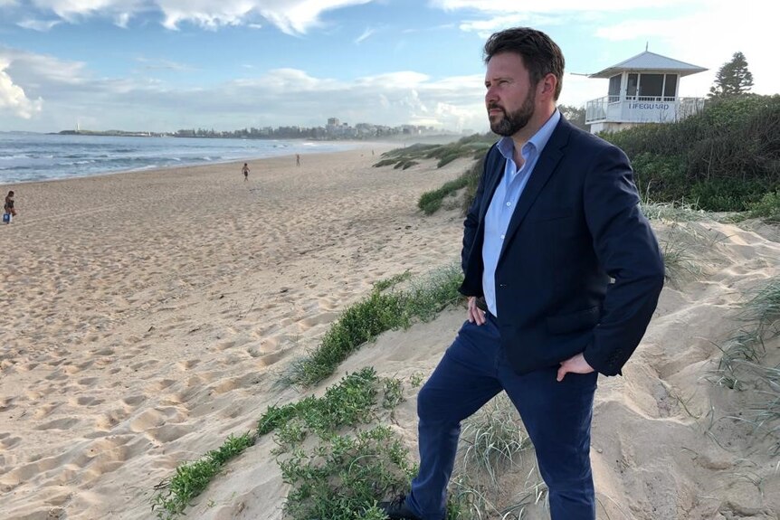 A man in a suit stands on a beach