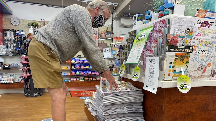 A country man in his 70s bends to buy a newspaper from local newsagency.