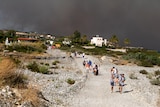 Tourists walk along a stony road in Rhodes as the sky behind them is filled with wildfire smoke
