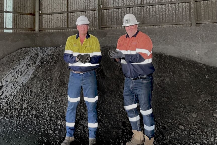 Two men wearing high-vis clothing and hard hats on a mine site holding nickel concentrate.