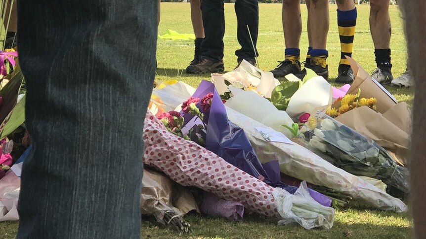 Footy players standing around a floral memorial for Eurydice Nixon, 22, who was killed on June 13, 2018.