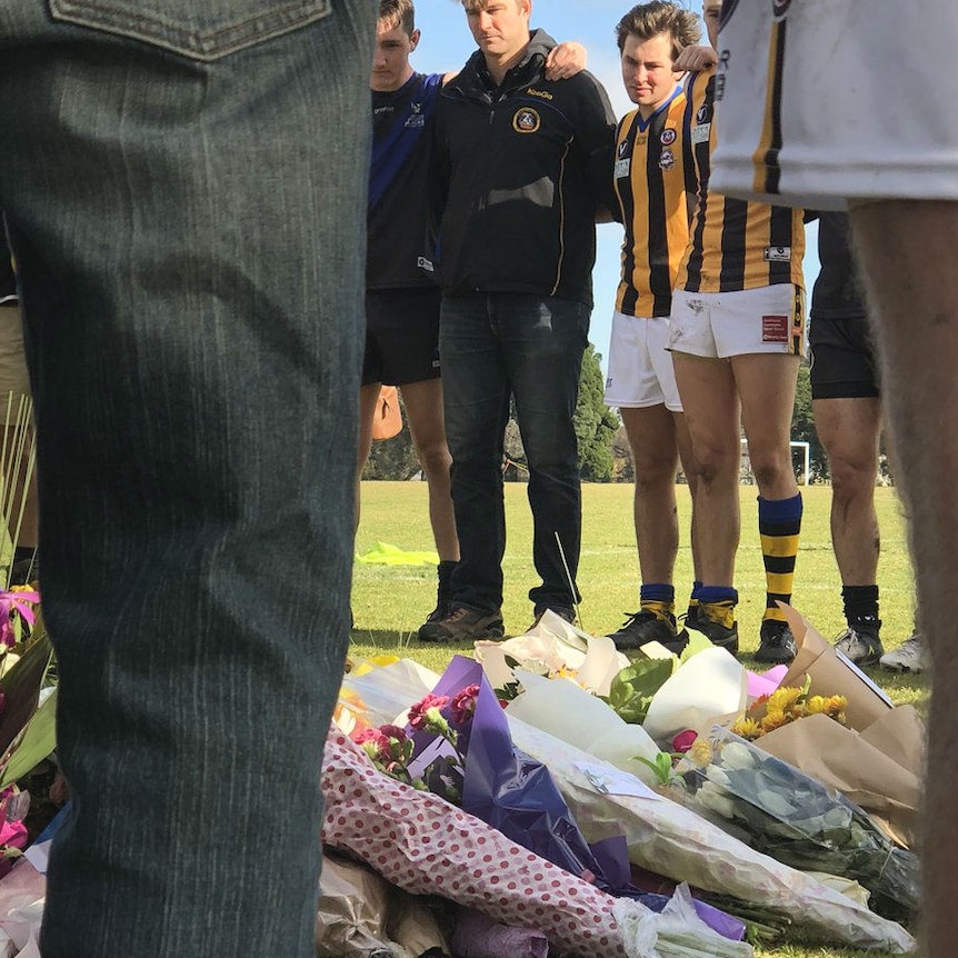 Footy players standing around a floral memorial for Eurydice Nixon, 22, who was killed on June 13, 2018.